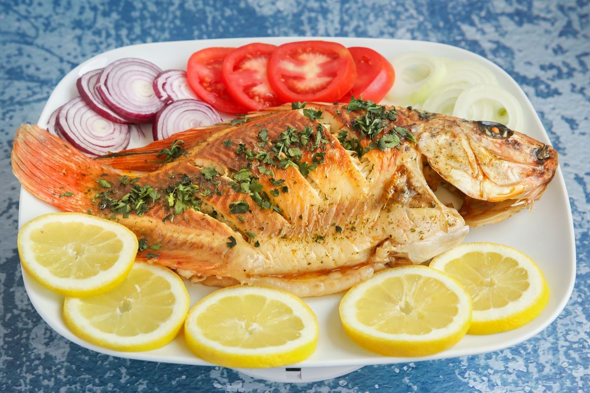 Whole fried fish garnished with tomato, onion and lemon